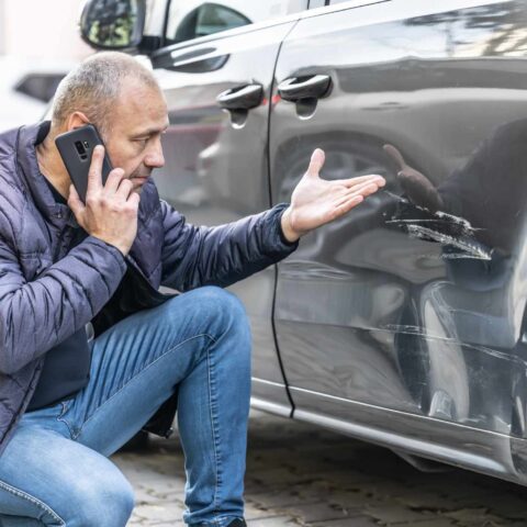 A man touches his damaged car as he wonders how to deal with a hit and run.