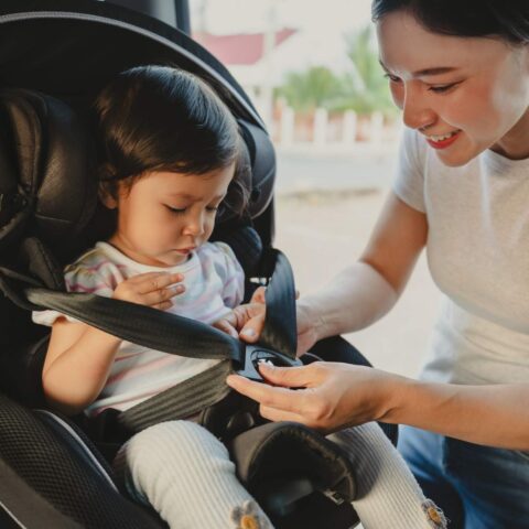 A mother straps her child into a car seat to comply with Minnesota car seat laws.